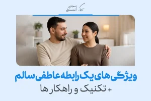 زوجی نشسته روی مبل با لبخند و نگاه صمیمی؛ نمادی از محبت و اعتماد در یک رابطه سالم عاطفی